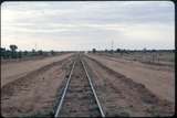 124181: Stuart Highway Level Crossing km 1292 5 Narrow Gauge Central Australia Railway looking South headlight of returning am train in extreme distance